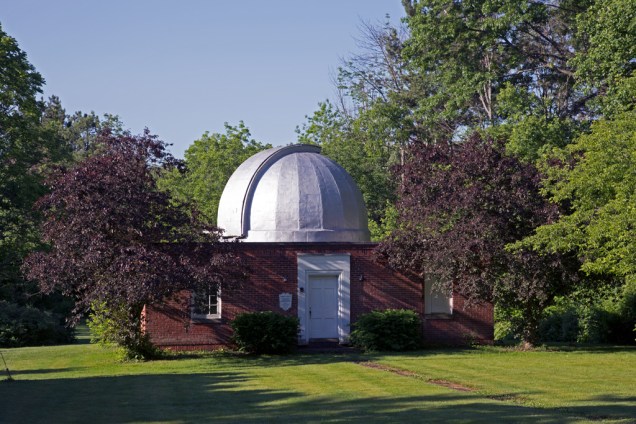 Stephens Memorial Observatory, its silver-painted dome brightly sunlit, on a sunny morning with trees in full leaf. Photo by James Guilford.