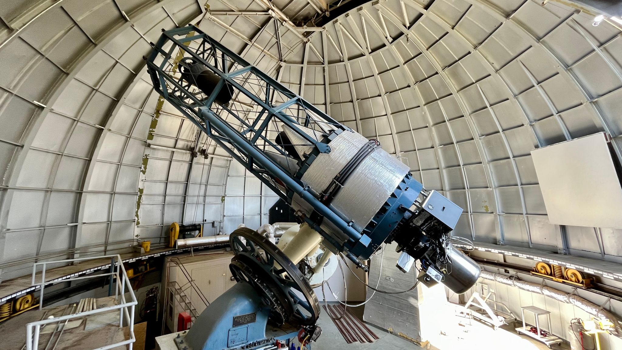 A large telescope sits beneath a spacious, ribbed, dome structure -- the observatory dome. The telescope has a solid mirror section attached to its mount, and an attached open section pointing skyward holding the telescope's secondary mirror.